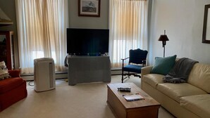 A living room with a flat-screen TV, a coffee table, a sofa, and a chair. - Charming 3rd Floor Walk-up River View (Clayton)