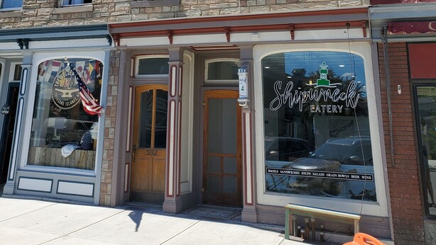 A multi-story building with a stone facade, large windows, and a storefront with a sign reading "Shipwreck Eatery". - Charming 3rd Floor Walk-up River View (Clayton)