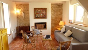 A cozy living room with a stone wall, a fireplace, wicker furniture, and a grey sofa. - Carnac, Charming holiday cottage for 2 people (Carnac)