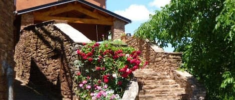 Staircase leads to a rustic building with a pitched roof, surrounded by lush greenery and flowering plants.