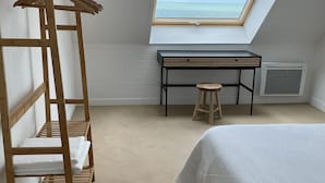 Une chambre avec une lucarne, une étagère en bois où sont posées des serviettes, un bureau et un lit.