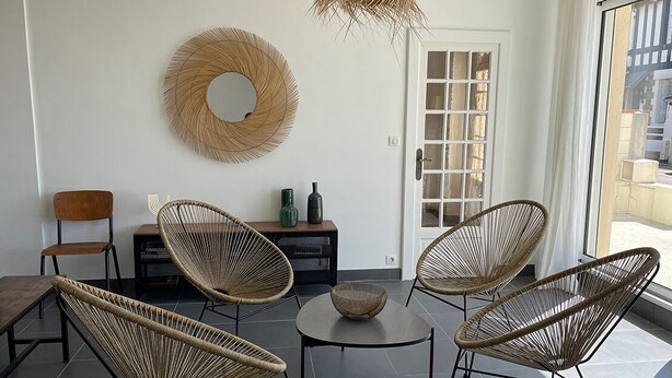 Un salon moderne avec des meubles en osier, un miroir rond et une petite table.