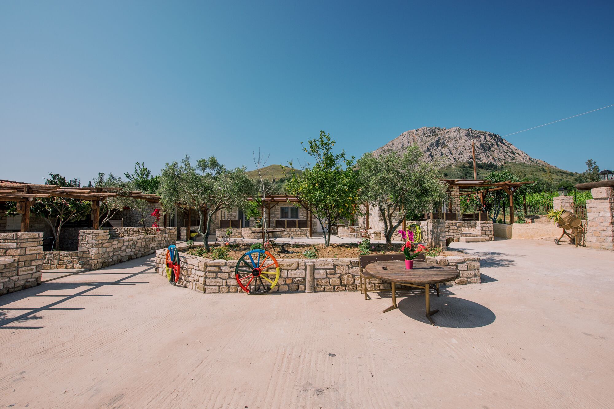 A courtyard with stone walls, a wooden pergola, and a table with chairs.