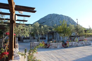 A stone building with a mountain in the background, a paved area with colorful wheels, and a wooden pergola with flowers.