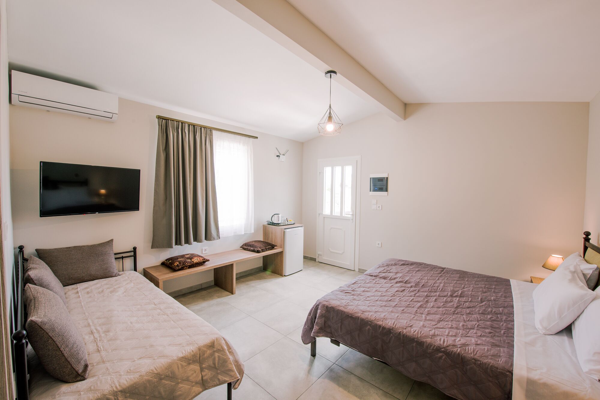 A bedroom with two beds, a TV, a desk, a window with curtains, and a door.