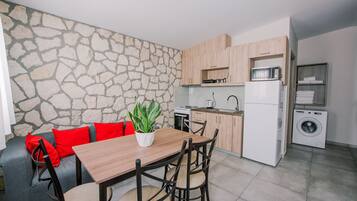 A compact kitchen with a stone wall, wooden cabinets, a microwave, a stove, and a washing machine.