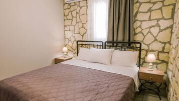 Une chambre avec un grand lit, un mur en pierre et une fenêtre avec des rideaux.