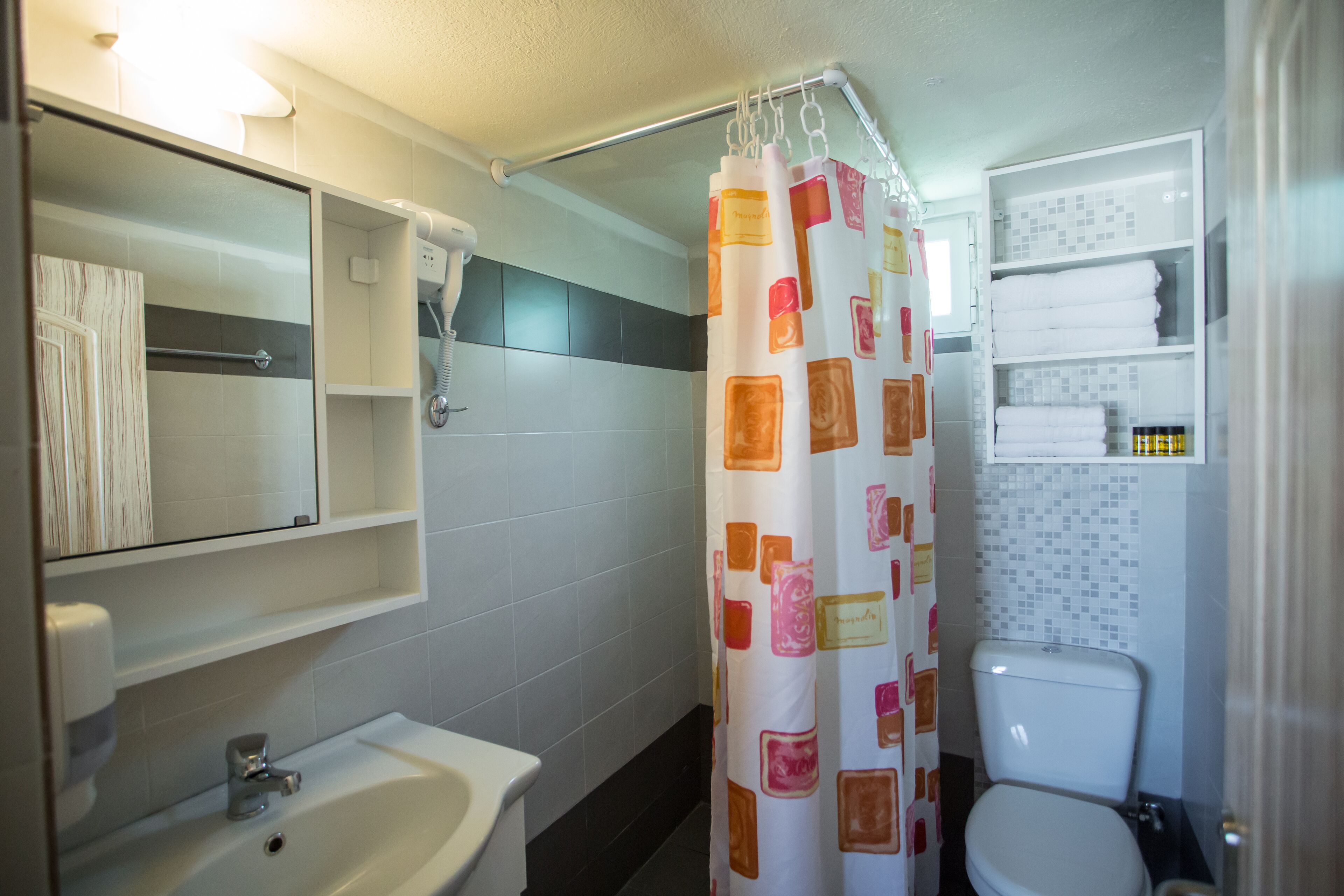 Un baño con lavamanos, espejo, toallero, cortina de ducha y retrete.