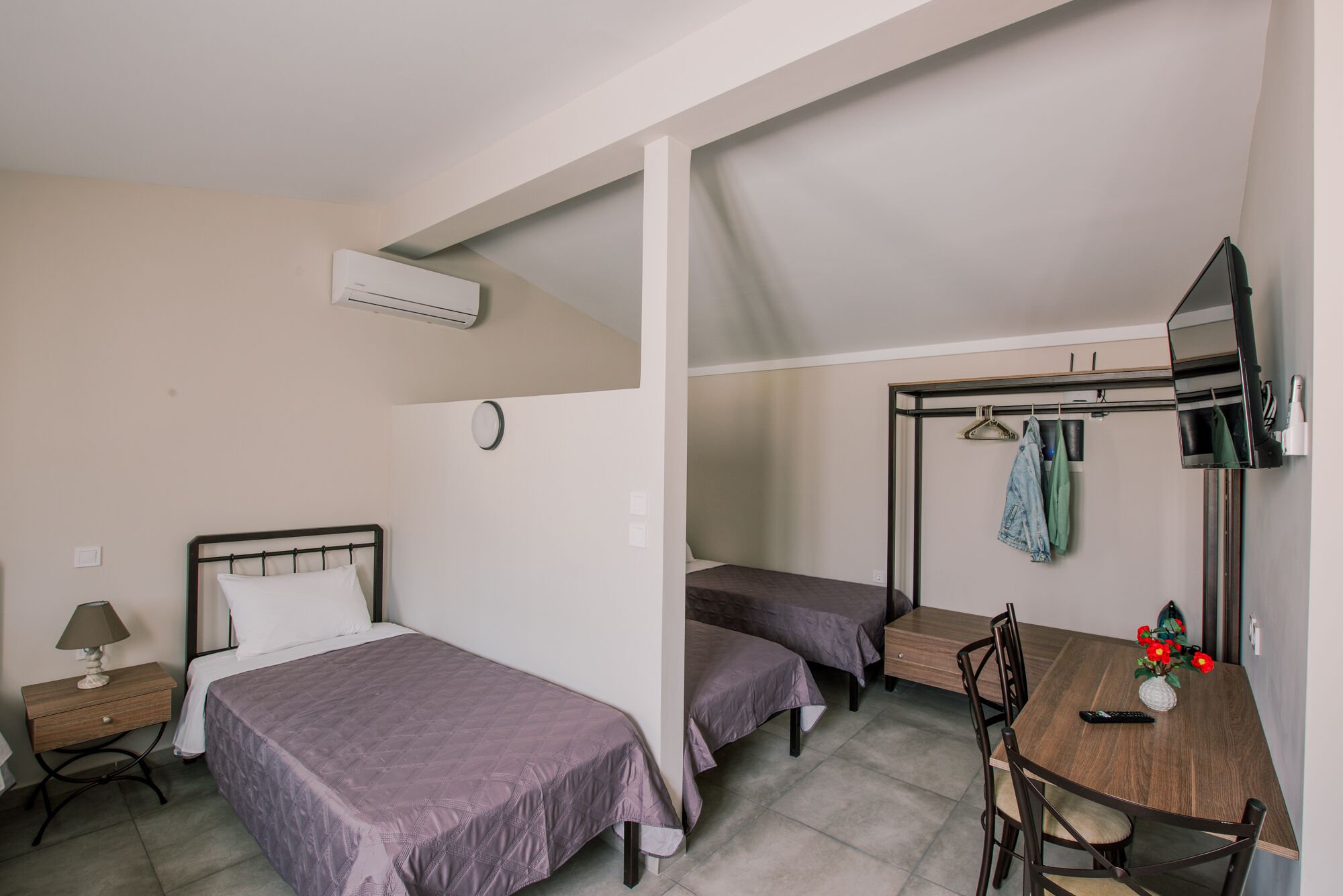 A room with two beds, a table, chairs, a TV, and a hanging clothes rack.
