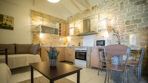 Uma sala de estar aconchegante com um sofá, uma mesa de centro e um espaço de jantar com cadeiras e uma mesa. Uma cozinha com fogão, forno e armários é visível ao fundo.
