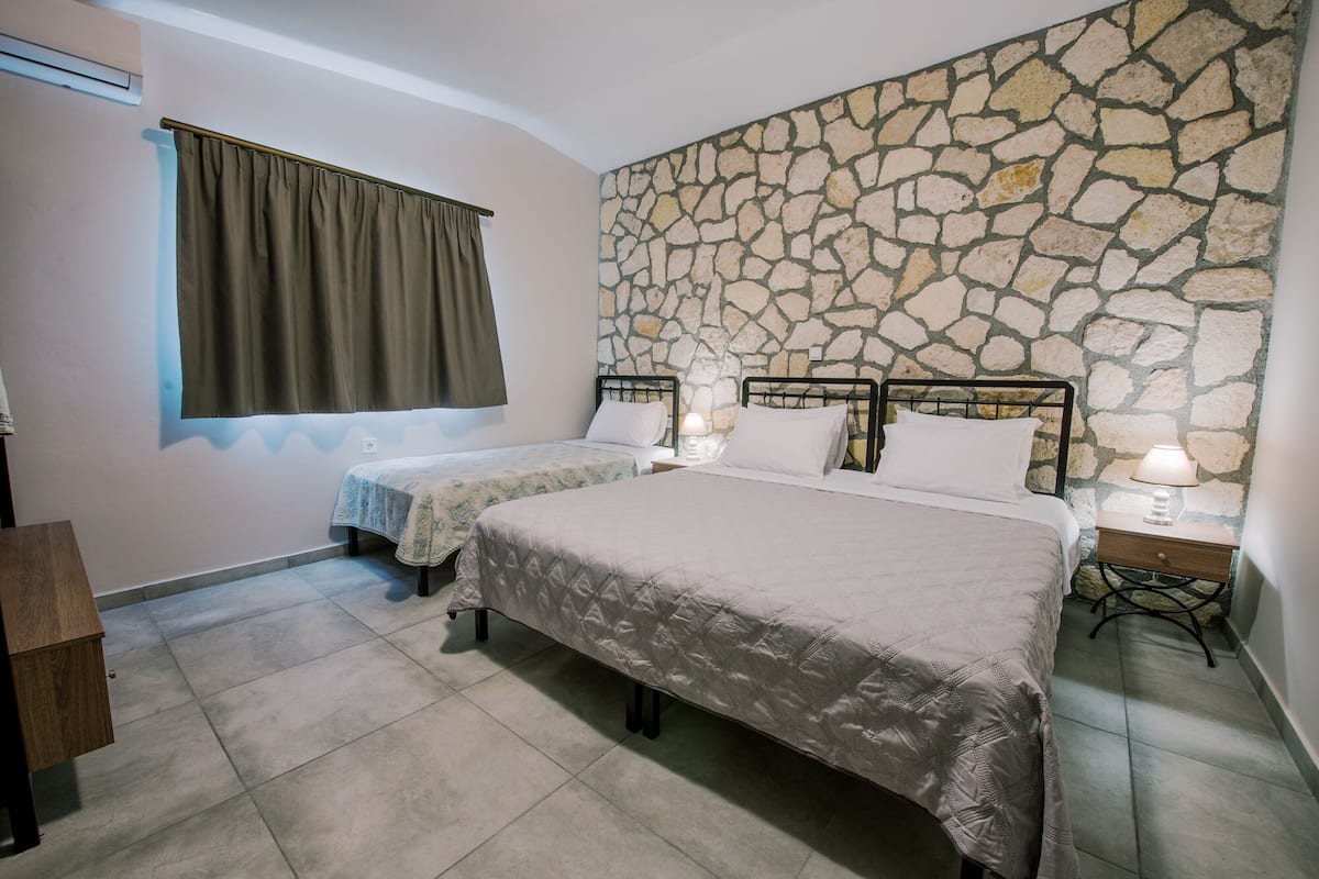 A bedroom with two beds, a stone wall, and a window with curtains.