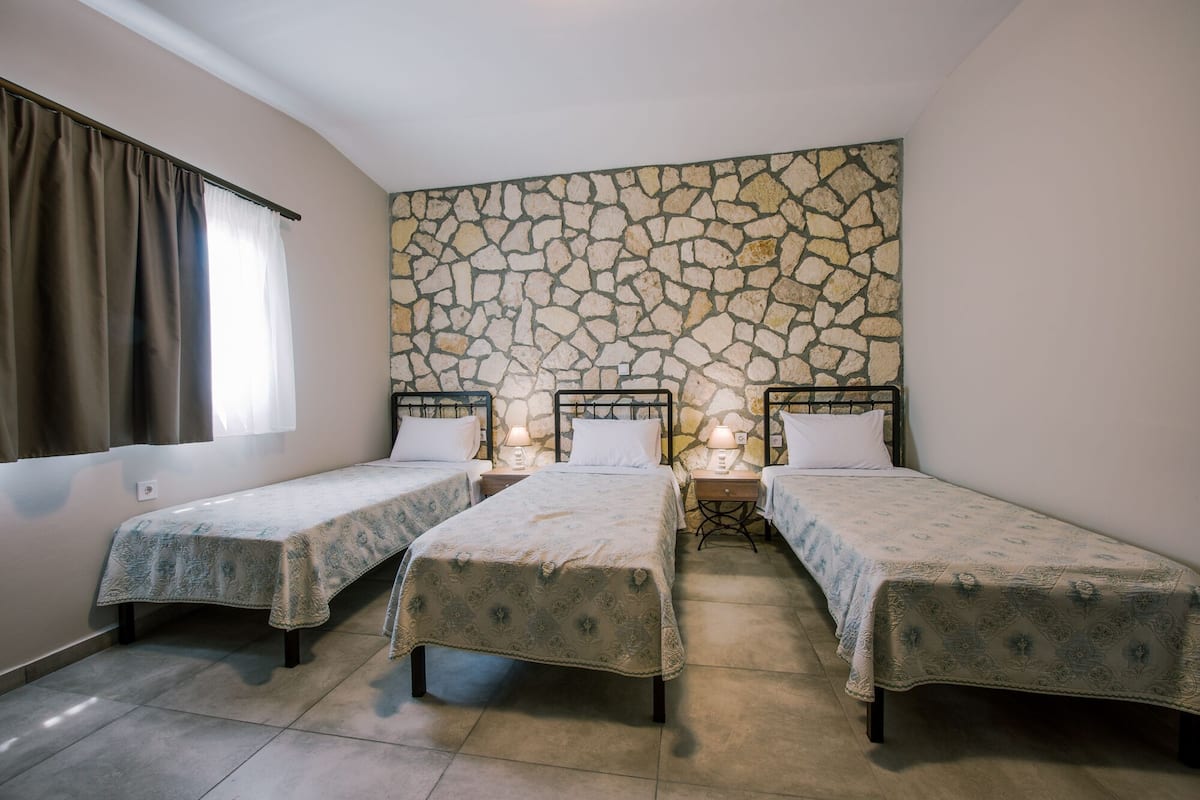 A room with three single beds, a stone wall, and a window with curtains.