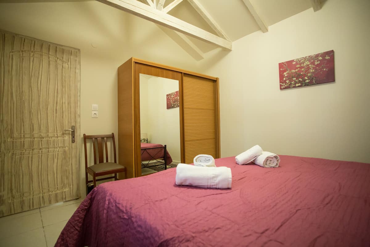 A bedroom with a bed, a wooden wardrobe, a chair, and a painting on the wall.