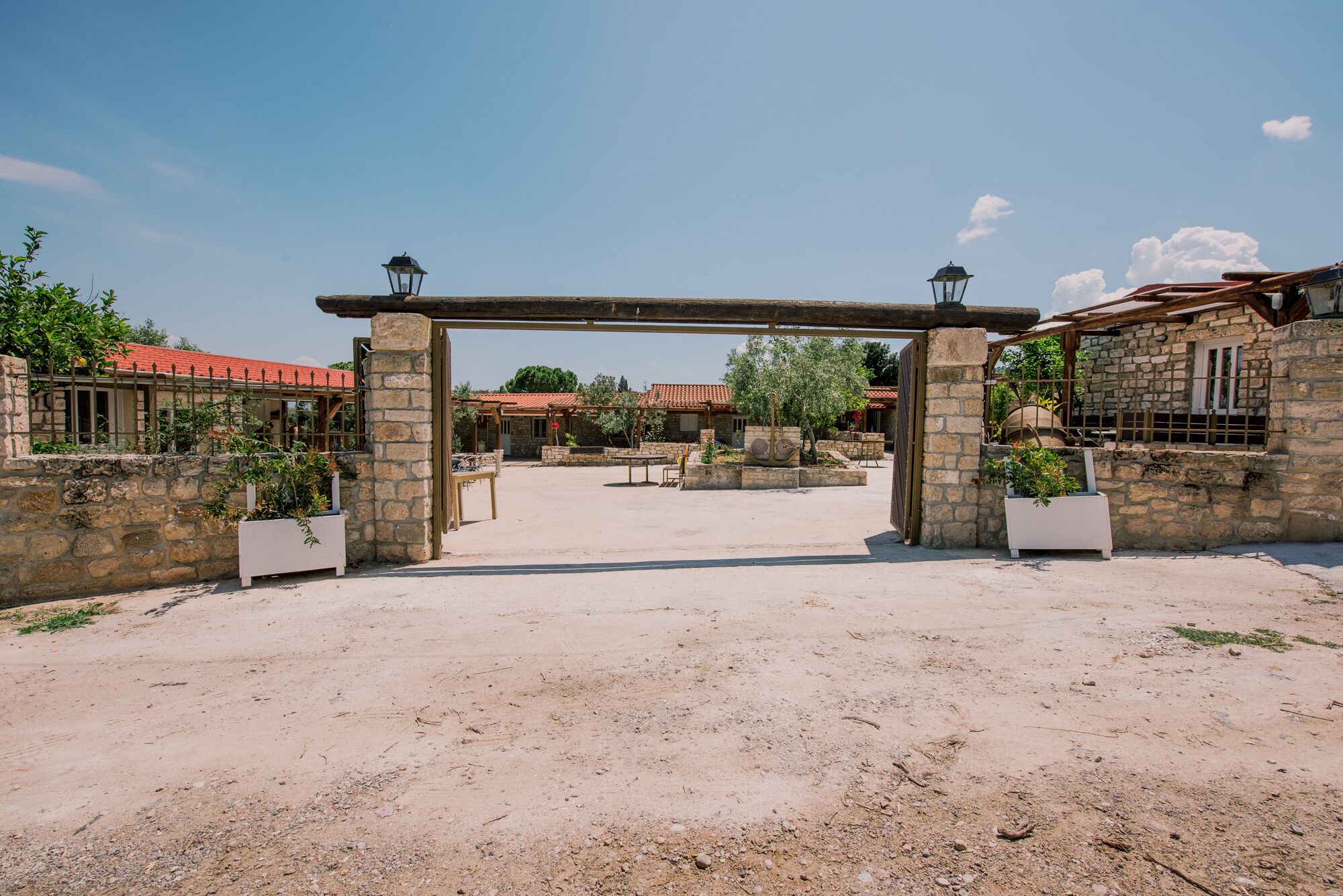 A courtyard with a stone archway, potted plants, and buildings with red-tiled roofs.