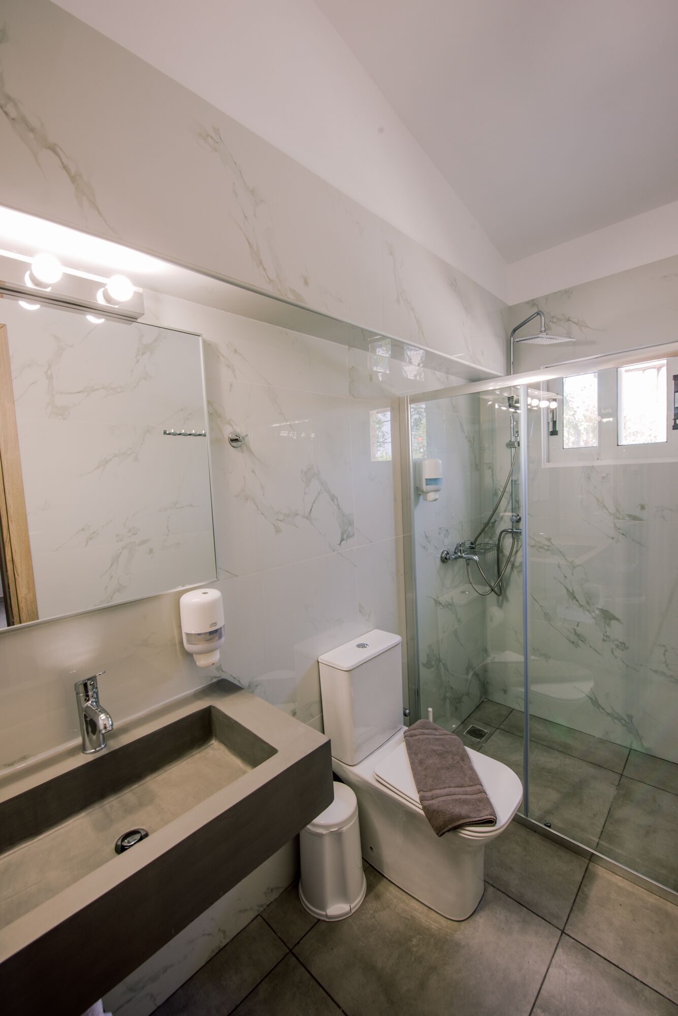 A modern bathroom with a marble sink, toilet, and glass-enclosed shower.