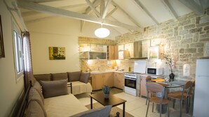 Uma sala de estar acolhedora com sofá e mesa de jantar, uma cozinha com parede de pedra e eletrodomésticos modernos, e um teto com vigas aparentes.