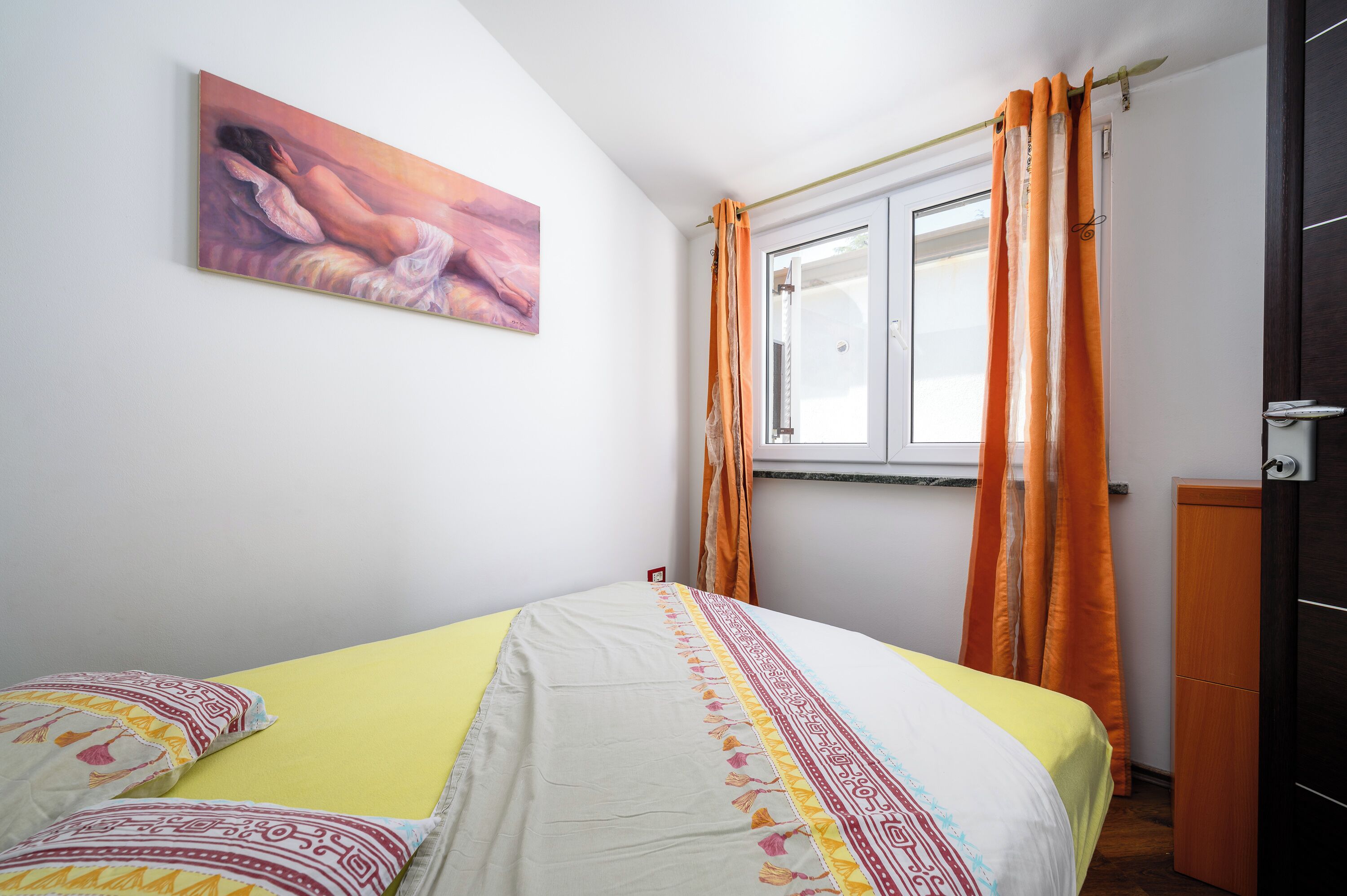 A bedroom with a bed, a painting, a window with curtains, and a wardrobe.