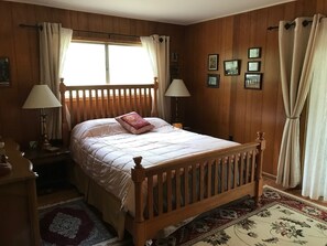 Un dormitorio con paneles de madera, una cama, dos lámparas de noche, una ventana con cortinas y una alfombra.