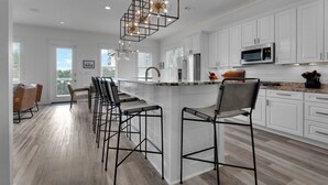 A modern kitchen with white cabinets, a central island with bar stools, a stainless steel microwave, and a pendant light fixture. - PRIVATE  POOL! 6 SEAT GOLF CART!  VOLLEYBALL COURT! 2 MIN. WALK TO BEACH! (Santa Rosa Beach)