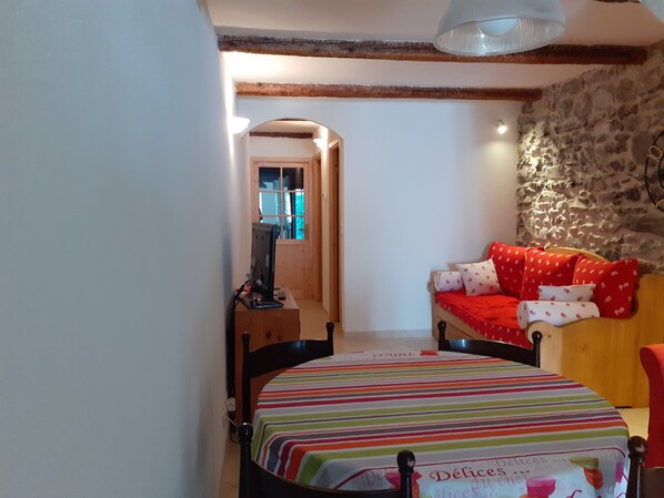 A cozy room with a bed, a wooden chair, a desk with a computer, and a stone wall.