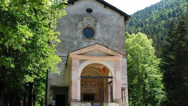 A rustic building with a central archway and a bell tower, surrounded by lush greenery and mountains. - Charmant Appartement de Village (La Brigue)