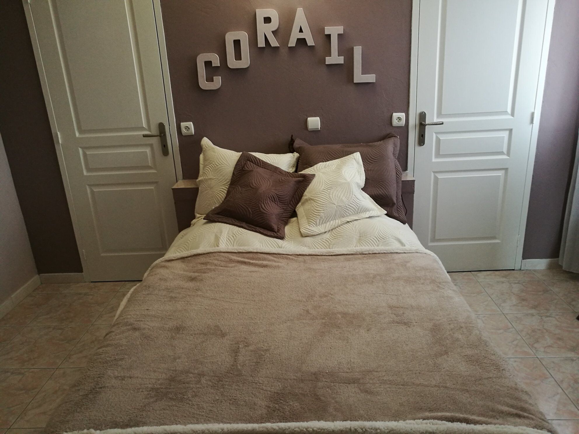 Ein Schlafzimmer mit einem Bett, zwei Kissen, einem Kopfteil mit der Aufschrift 'CORAIL' und zwei Türen.