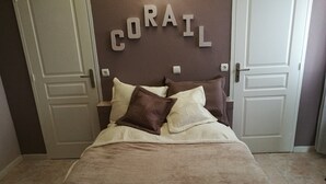 Et soveværelse med en seng, to puder, en sengegavl med ordet "CORAIL" og to døre.