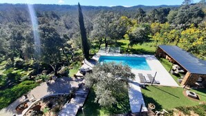 A swimming pool surrounded by a deck with outdoor seating, a covered area, and a view of a forested landscape.