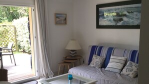 Un salon avec un canapé, une table basse, un fauteuil en osier, une lampe et un tableau accroché au mur.
