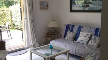 Een woonkamer met een bank, een salontafel, een rieten stoel, een lamp en een schilderij aan de muur.