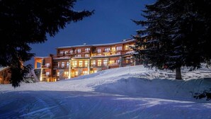 Ett hotell med flera våningar, med en skidbacke i förgrunden, upplysta fönster och ett snötäckt landskap runt omkring.