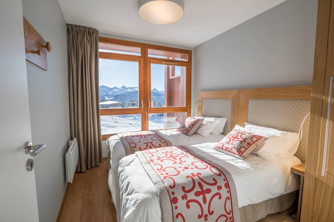 Habitación de hotel con dos camas, un ventanal grande con vista a la montaña, cabecero de madera y un radiador.