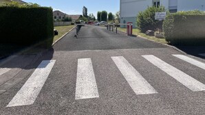 Un camino de entrada con portón que conduce a un edificio residencial, bajo un cielo despejado.