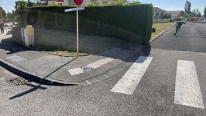 Una señal de alto en una intersección, con un seto y un edificio al fondo.