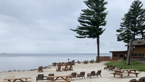 A beach with wooden benches and picnic tables, a grassy area, and a building in the background.