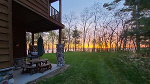 A wooden cabin with a stone pillar and a barbecue grill outside.