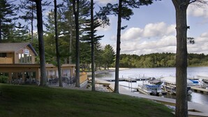 A lakeside cabin with a dock, surrounded by tall trees and a grassy area.