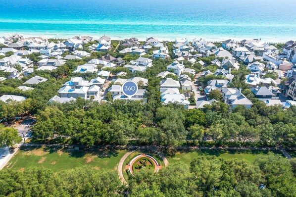 Vue aérienne d’un quartier résidentiel situé sur la côte, avec des maisons, un parc circulaire et une vue dégagée sur l’océan.