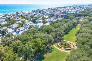 An aerial view of a coastal residential area with houses, a golf course, and a large body of water.