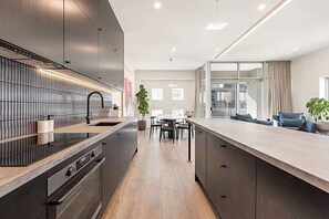 A modern kitchen with a central island, built-in appliances, and a dining area with a view. - Incredible Balcony Duplex in the Heart of Fitzroy (Fitzroy)