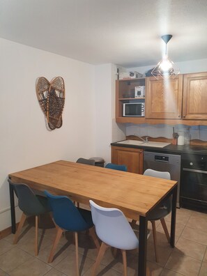 Una cocina con armarios de madera, microondas y lavavajillas. Hay una mesa de comedor con sillas azules y blancas.