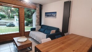 Une pièce chaleureuse avec une table en bois, un canapé bleu et une grande fenêtre donnant sur l’extérieur.