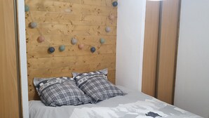 Une chambre à coucher avec une tête de lit en bois, deux coussins à carreaux et un lit recouvert d’une couvre-lit blanche et grise à motifs.