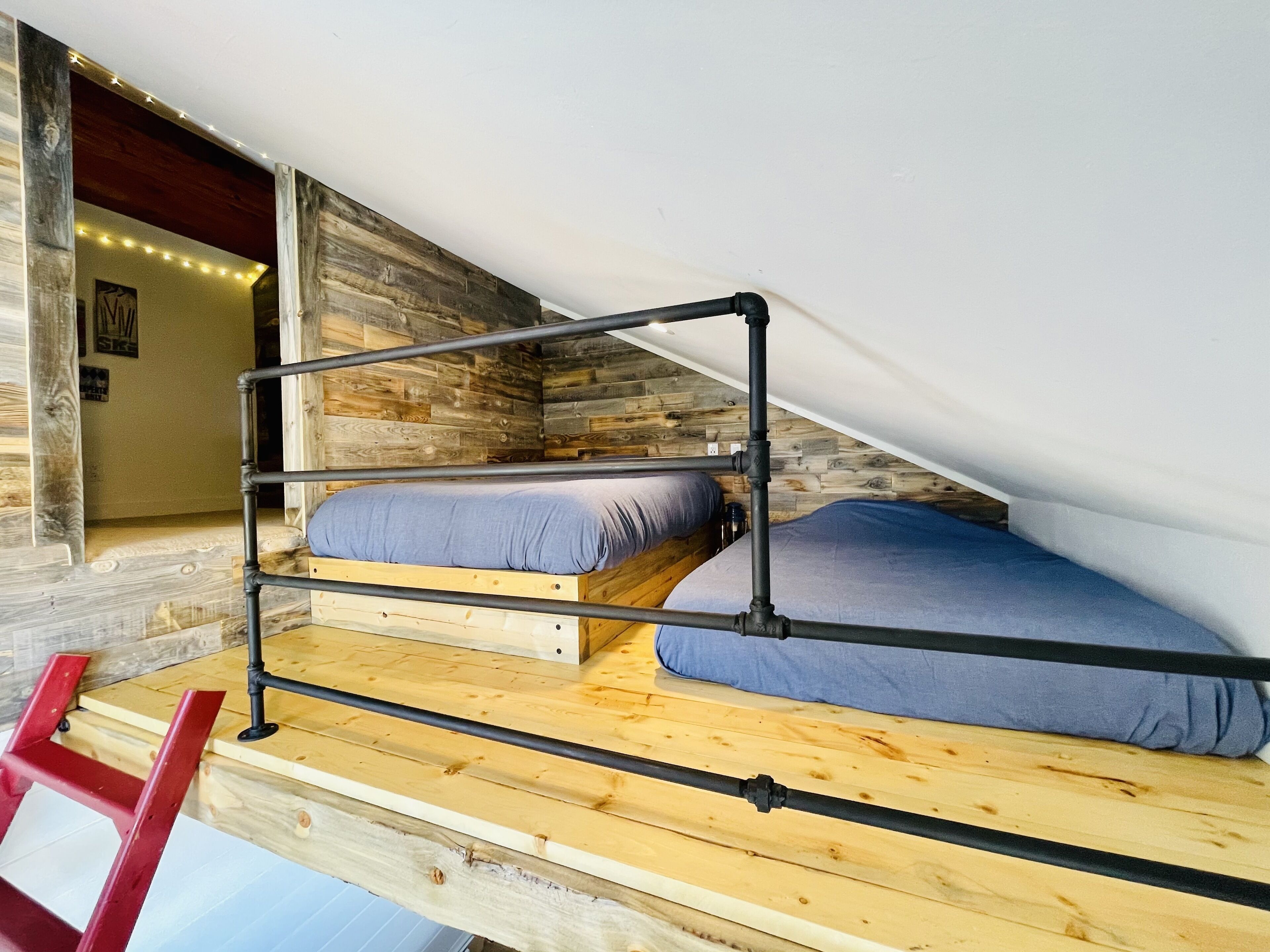 Un dormitorio estilo loft con suelo de madera, una cama litera y una escalera roja.