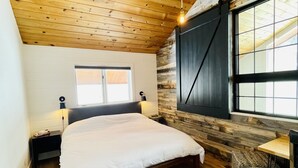 Une chambre avec un plafond en bois, un lit, une table de chevet, une fenêtre et un téléviseur fixé au mur.