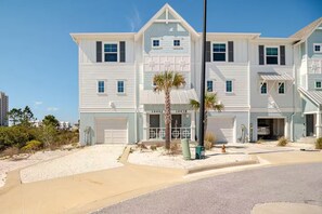 A multi-story residential building with a garage, a covered front porch, and a small palm tree.
