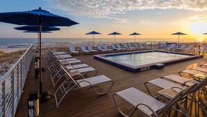 Un espace piscine ensoleillé, doté de chaises longues et de parasols, avec vue sur l’océan.