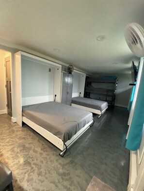 Compact accommodation with two foldable beds, a small table, and a wall-mounted fan for a functional stay.