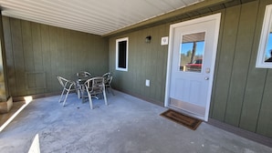 Un espacio exterior techado con una mesa, sillas, una puerta y una ventana.
