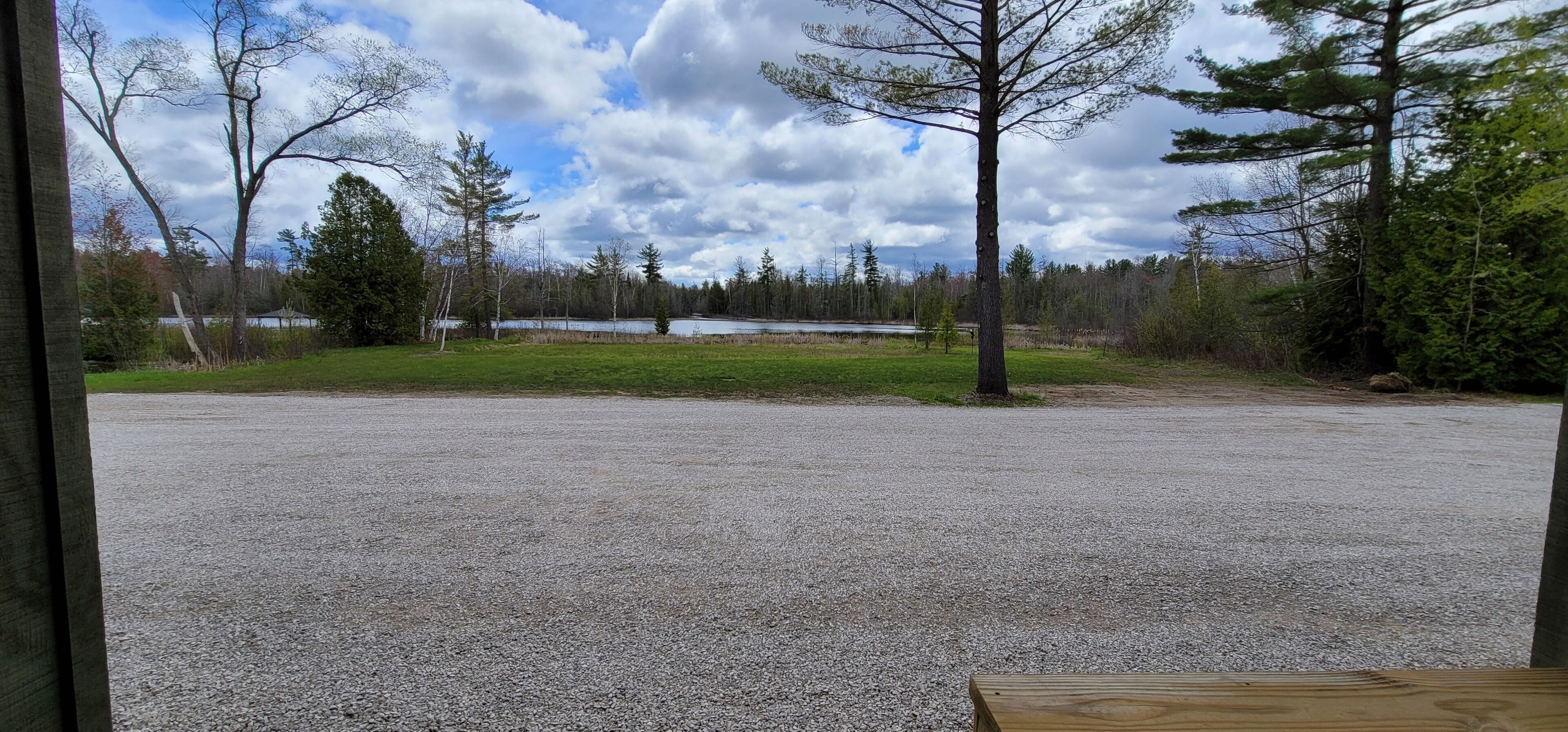 Un espace de stationnement recouvert de gravier, offrant une vue sur un lac et une forêt.